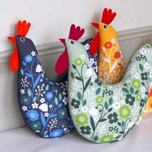 Colourful chicken-shaped cushions with floral patterns on a light background.